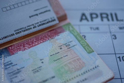 H1B visa (for specialty workers) stamp in passport, blurred april calendar on background. H1B visa program deadline concept. Close up view.