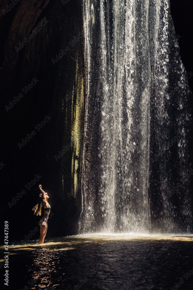 Obraz premium girl standing in the sunlight in a cave with a waterfall