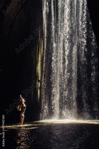 Fototapeta Naklejka Na Ścianę i Meble -  girl standing in the sunlight in a cave with a waterfall