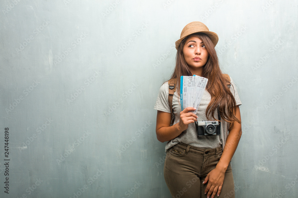 Portrait of young traveler latin woman against a wall doubting and confused, thinking of an idea or worried about something. Holding a boarding pass. Portrait of young traveler latin woman against a wall doubting and confused, thinking of an idea or worried about something. Holding a boarding pass.
