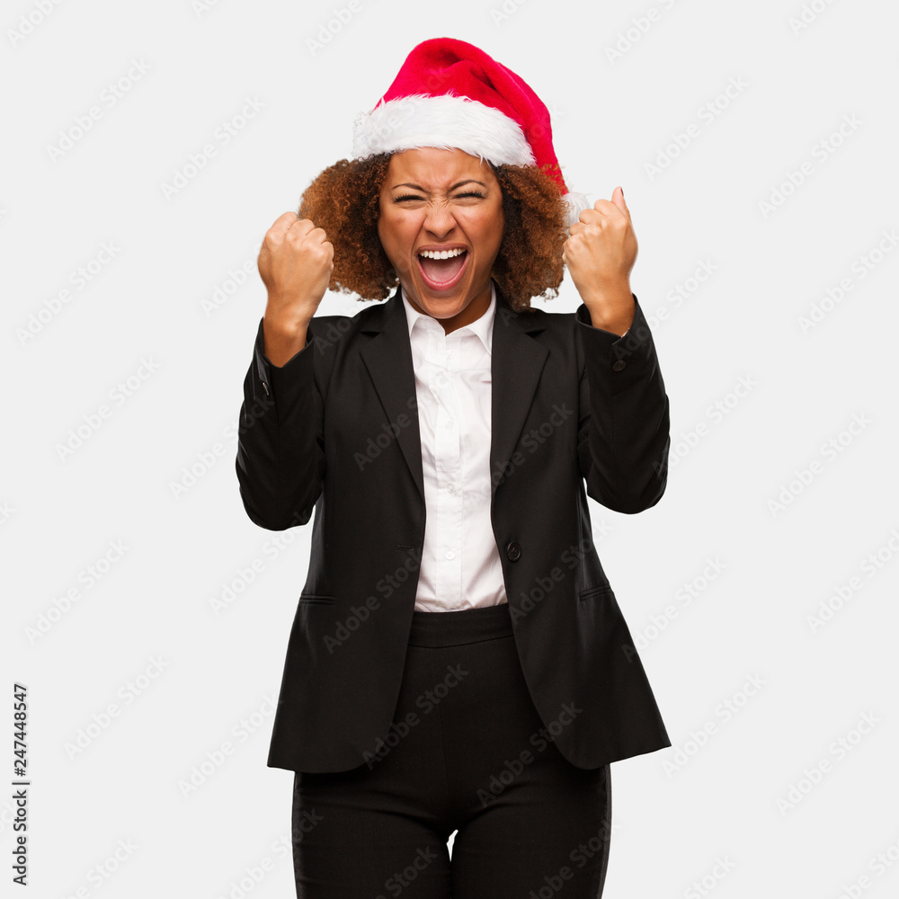 Young business black woman wearing a chirstmas santa hat screaming very angry and aggressive Young business black woman wearing a chirstmas santa hat screaming very angry and aggressive