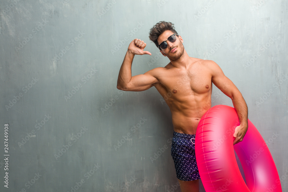 Young athletic man wearing a swimsuit against a grunge wall proud and confident, pointing fingers, example to follow, concept of satisfaction, arrogance and health