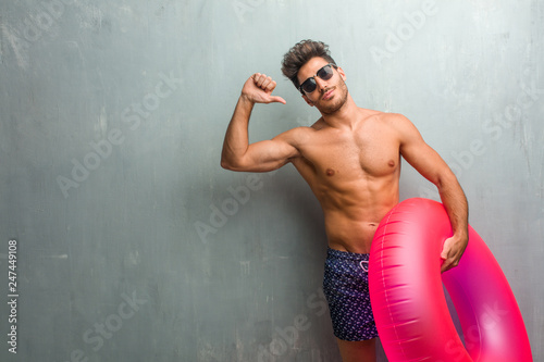 Obraz na płótnie Young athletic man wearing a swimsuit against a grunge wall proud and confident,