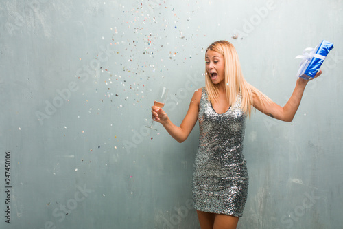 Elegant young blonde woman celebrating new year with champagne, one gift and confetti. © Asier