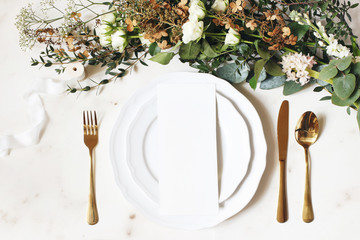 Festive wedding, birthday table setting with golden cutlery, silk ribbon, eucalyptus branches, hydrangea and white roses flowers. Blank card mockup. Restaurant menu concept. Flat lay, top view