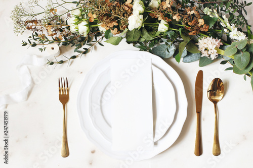 Festive wedding, birthday table setting with golden cutlery, silk ribbon, eucalyptus branches, hydrangea and white roses flowers. Blank card mockup. Restaurant menu concept. Flat lay, top view