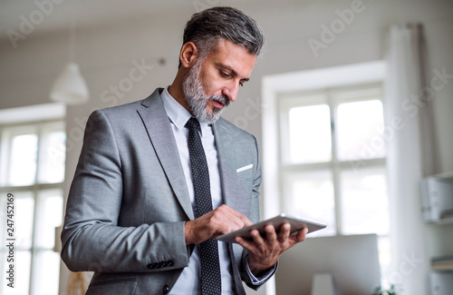 A mature businessman standing in an office, using tablet. photo