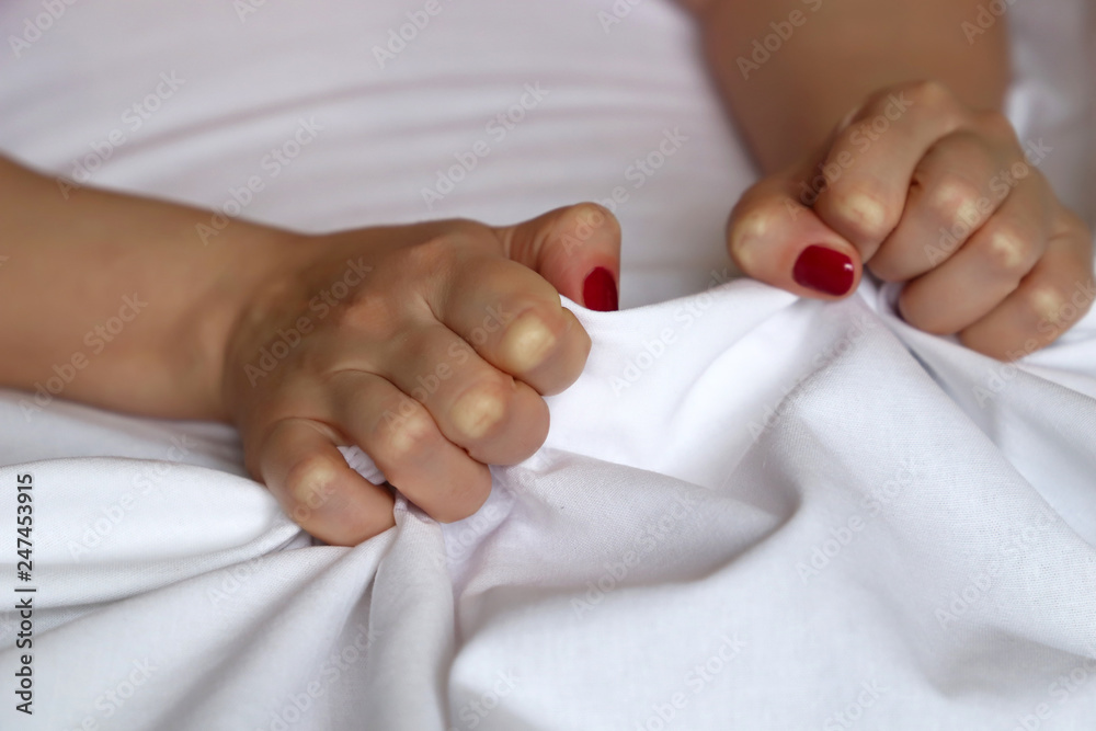 Female hands with red nails pulling and gripping white bedsheet in ecstasy pic