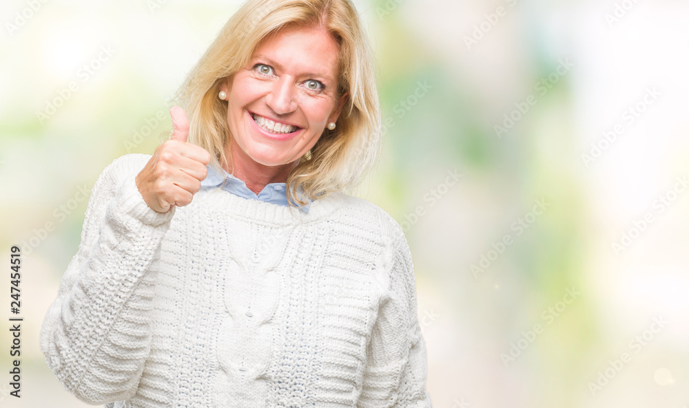 Middle age blonde woman wearing winter sweater over isolated background doing happy thumbs up gesture with hand. Approving expression looking at the camera with showing success.
