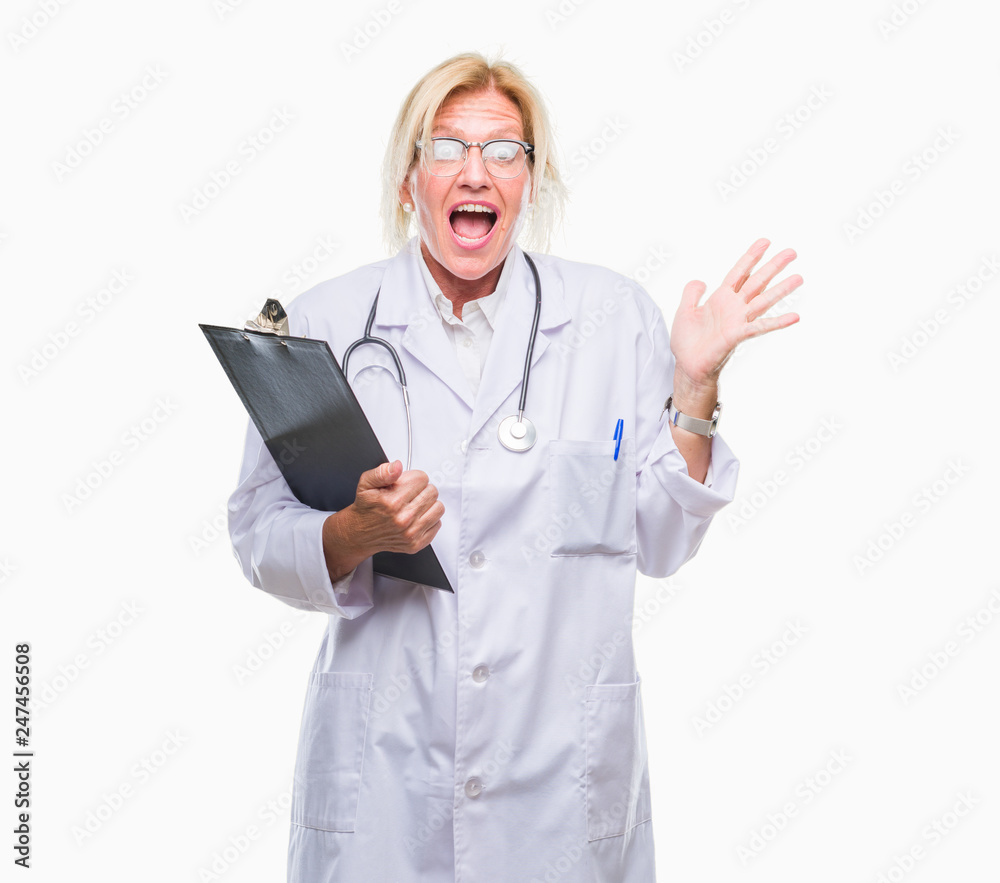 Middle age blonde doctor woman holding clipboard over isolated background very happy and excited, winner expression celebrating victory screaming with big smile and raised hands Middle age blonde doctor woman holding clipboard over isolated background very happy and excited, winner expression celebrating victory screaming with big smile and raised hands