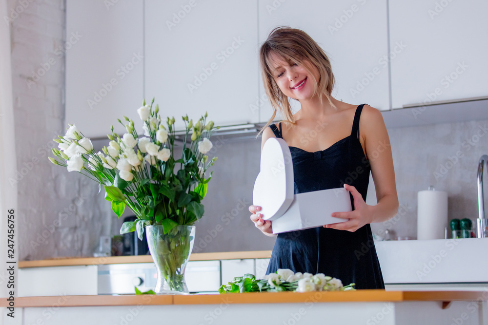 a woman dressed in a black dress near white roses bouquet in a vase holding heart shape box. Valentines Day concept a woman dressed in a black dress near white roses bouquet in a vase holding heart shape box. Valentines Day concept