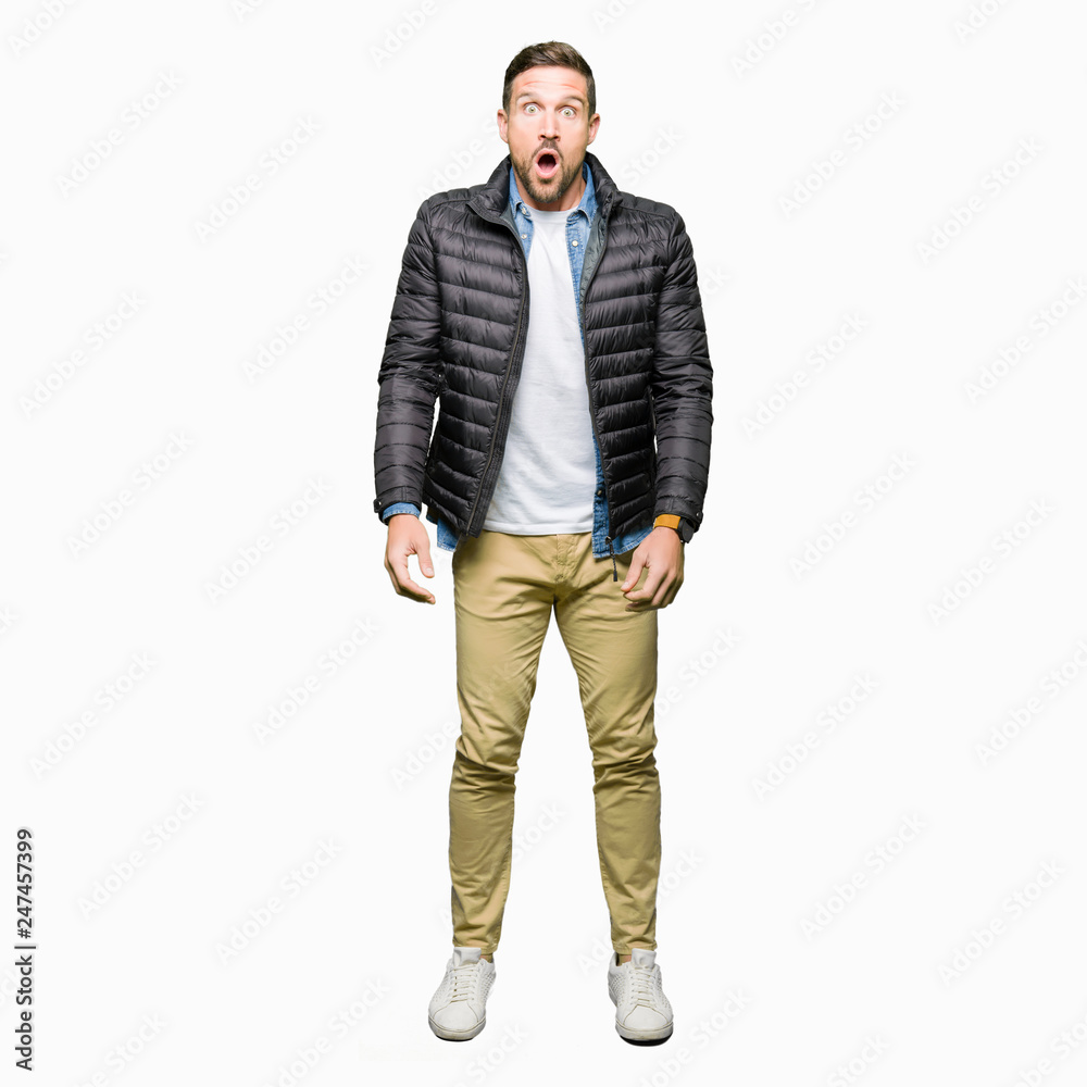 Handsome man wearing winter coat afraid and shocked with surprise expression, fear and excited face.