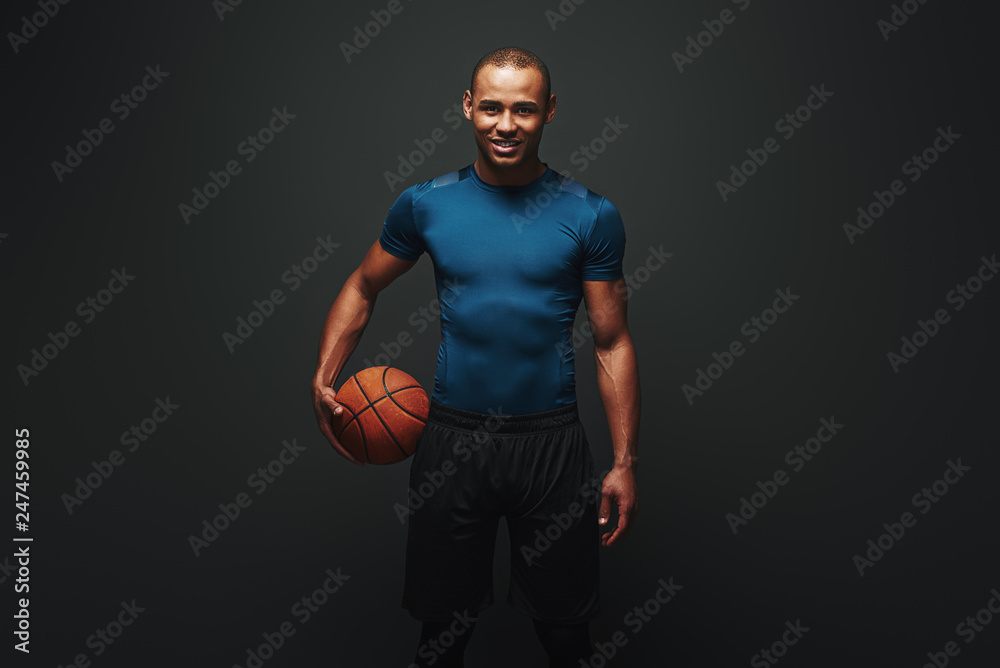 Fototapeta premium He is a new champion. Handsome sportsman standing over dark background with basketball ball in his hand