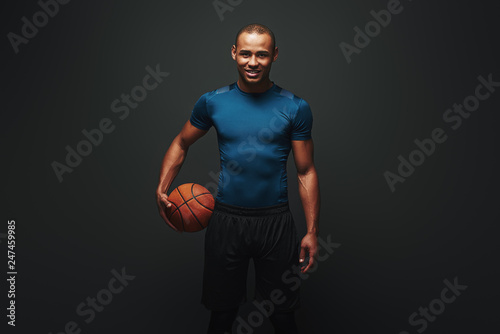 He is a new champion. Handsome sportsman standing over dark background with basketball ball in his hand © Friends Stock