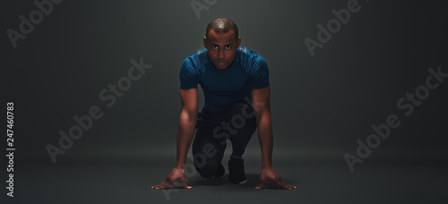 At the start! Young sportsman is ready to run standing over dark background photo