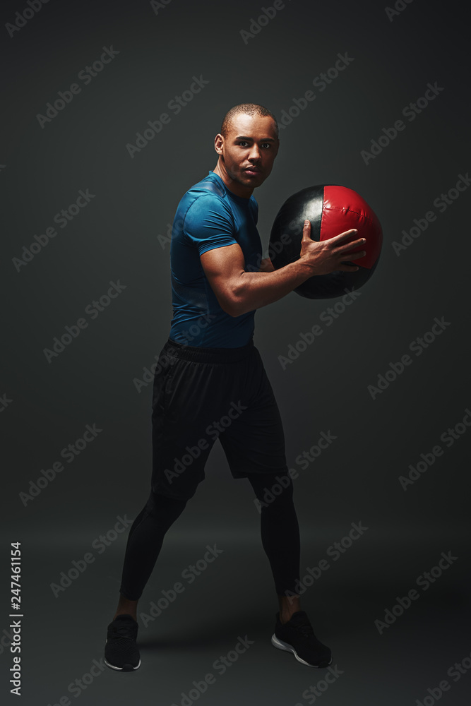 Training hard. Young sportsman standing over dark background with a ball in his hands