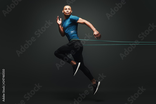 I can do it. Sportsman jumping with resistance band over dark background, looking away