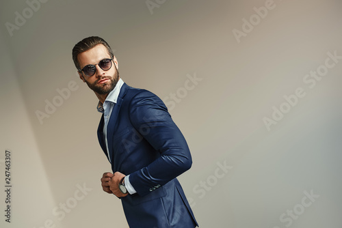 Handsome businessman at office. Bearded sexy man in a stylish suit and sunglasses is standing at office and looking away