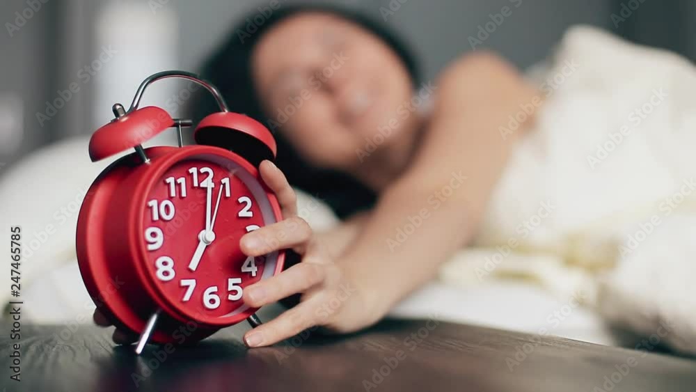 Woman turning off alarm clock lying in bed morning wake up happy smile