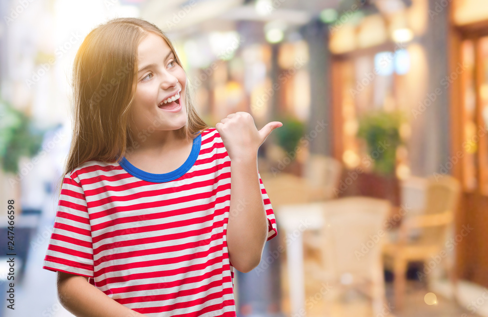 Young beautiful girl over isolated background smiling with happy face looking and pointing to the side with thumb up.