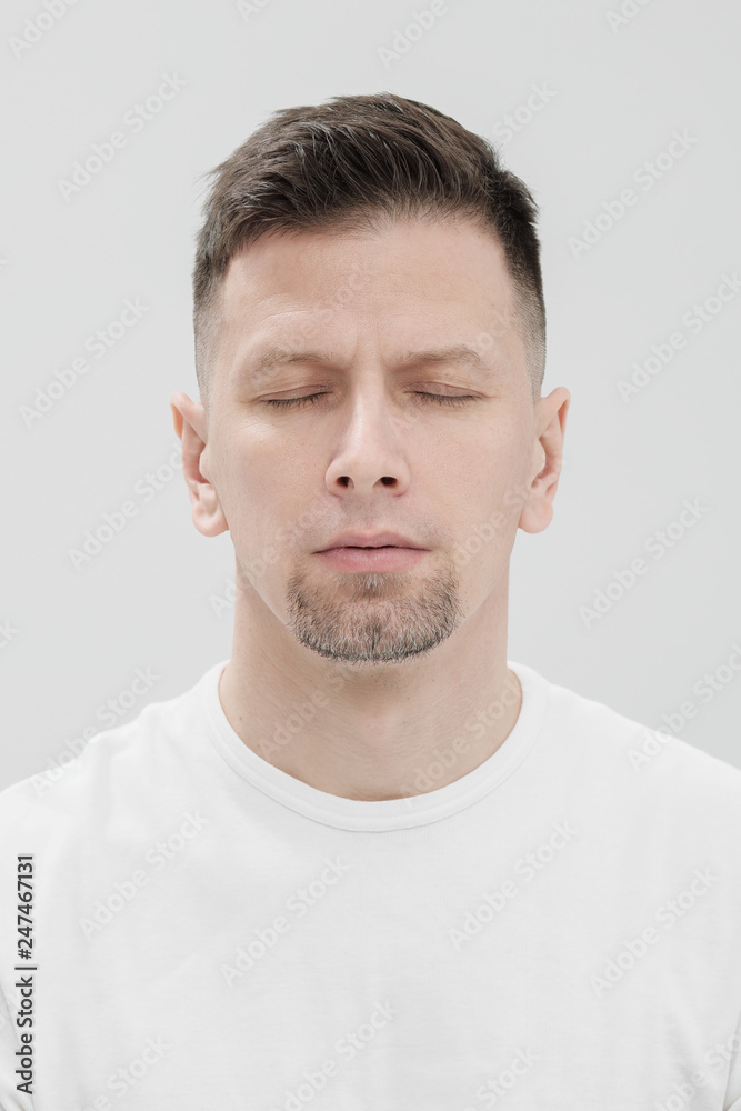 The face of a bearded brunet man in white clothes, eyes closed close up. The face of a bearded brunet man in white clothes, eyes closed close up.