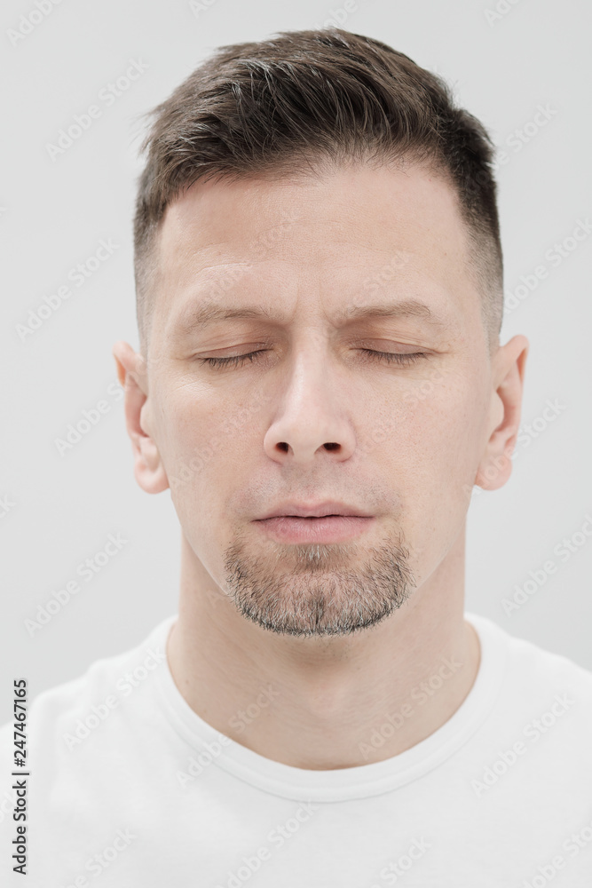 The face of a bearded brunet man in white clothes, eyes closed close up.