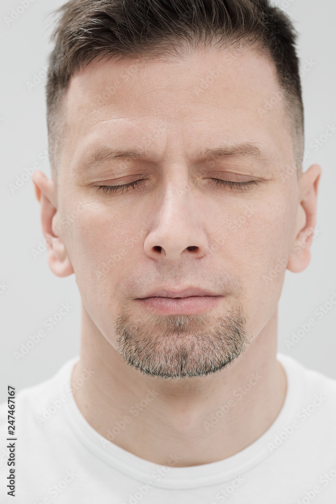 The face of a bearded brunet man in white clothes, eyes closed close up. The face of a bearded brunet man in white clothes, eyes closed close up.