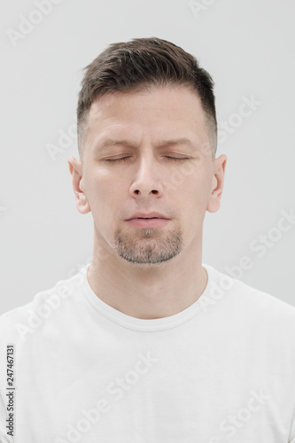 The face of a bearded brunet man in white clothes, eyes closed close up.