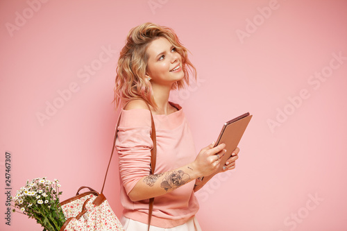 Fotografi Young smiling hipster student woman with curly colored pink hairstyle and tattoo holding tablet