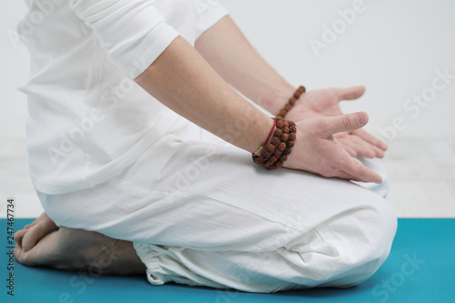 Concept of yoga and meditation. Close-up, hands of a man in white clothes, folded in prayer. White background and yellow-mini rubber mat.