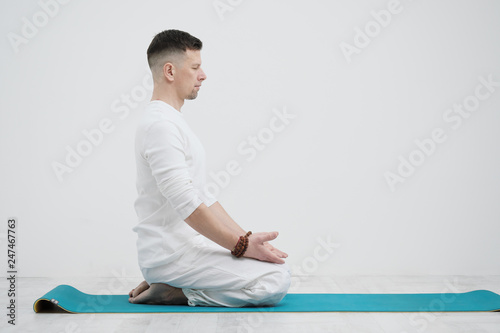 Male brunette with a beard in white clothes on a white background with his hands folded on his chest. Meditation and prayer, yoga.