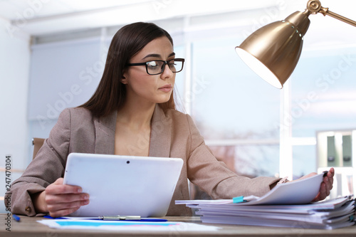 Businesswoman working with tablet and documents at table in office