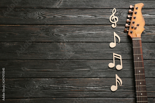 Music notes and guitar neck on wooden background, top view. Space for text