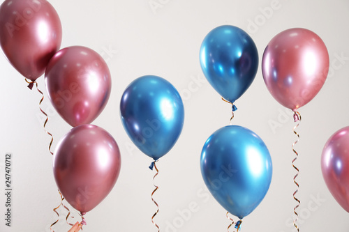 Bright balloons with ribbons flying on light background