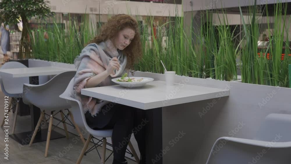 young beautiful woman with red curly hair eats Caesar salad in a cafe young beautiful woman with red curly hair eats Caesar salad in a cafe