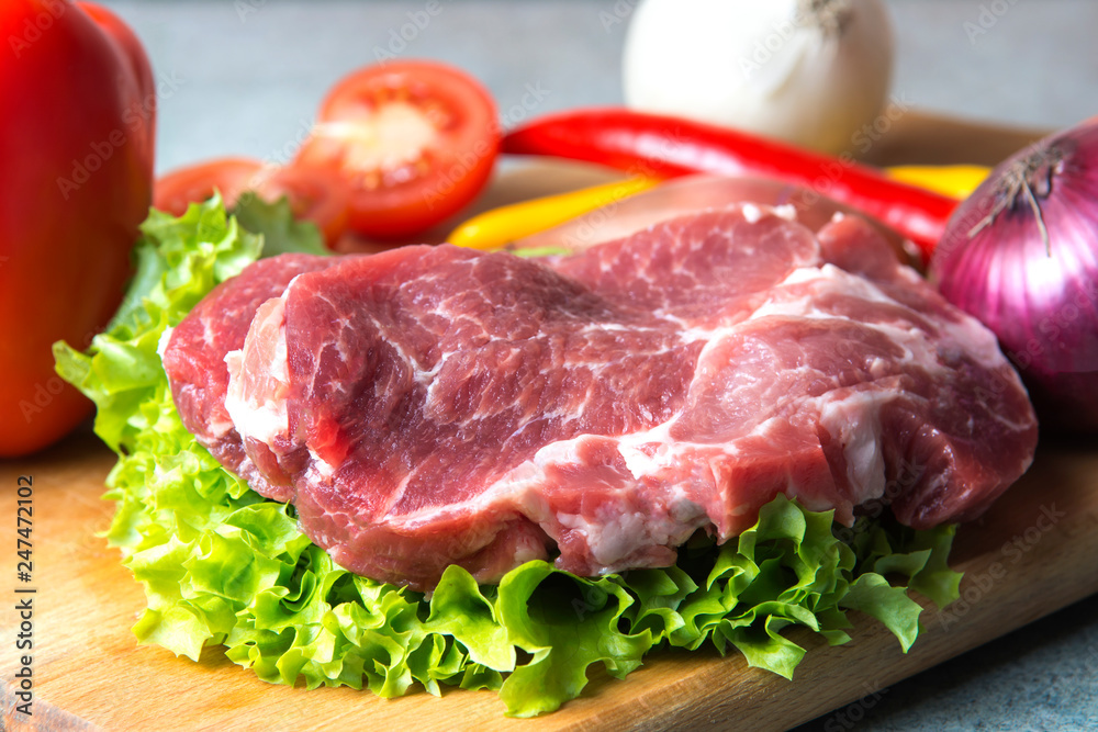 Pork-neck meat steaks on lettuce on background of radishes, tomato, red chili peppers, yellow chili peppers, green paprika, yellow paprika, red paprika, black pepper. Horizontal. Red onions, shallots