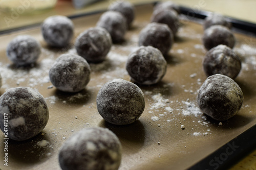Small brown chocolate balls lay on a baking sheet sprinkled with powdered sugar and flour