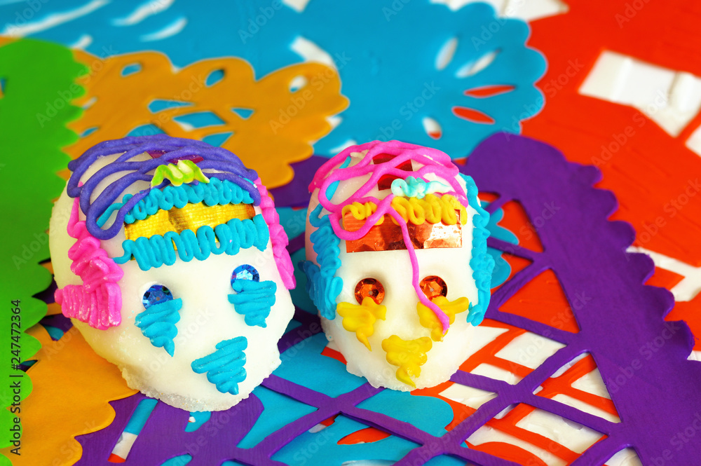couple of sugar skulls on orange yellow purple green and blue perforated paper