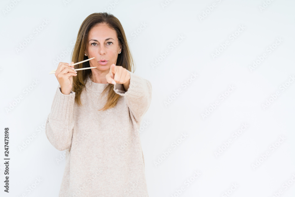 Middle age woman holding asian chopsticks over isolated background pointing with finger to the camera and to you, hand sign, positive and confident gesture from the front Middle age woman holding asian chopsticks over isolated background pointing with finger to the camera and to you, hand sign, positive and confident gesture from the front