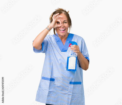 Middle age brunette cleaner woman wearing housework uniform over isolated background with happy face smiling doing ok sign with hand on eye looking through fingers