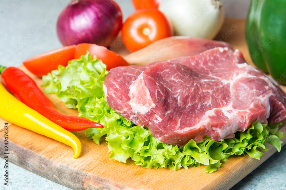 Pork-neck meat steaks on lettuce on background of radishes, tomato, red chili peppers, yellow chili peppers, green paprika, yellow paprika, red paprika, black pepper. Horizontal. Red onions, shallots Pork-neck meat steaks on lettuce on background of radishes, tomato, red chili peppers, yellow chili peppers, green paprika, yellow paprika, red paprika, black pepper. Horizontal. Red onions, shallots