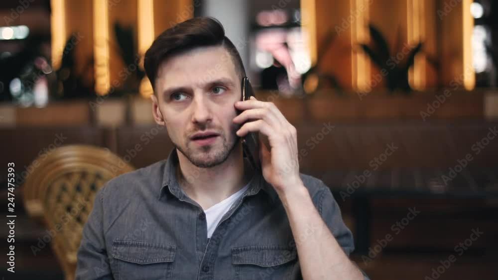 Portrait view of surprised man wearing casual outfit listening shocking news from his interlocutor while speaking on the smartphone at the cafe interior Portrait view of surprised man wearing casual outfit listening shocking news from his interlocutor while speaking on the smartphone at the cafe interior