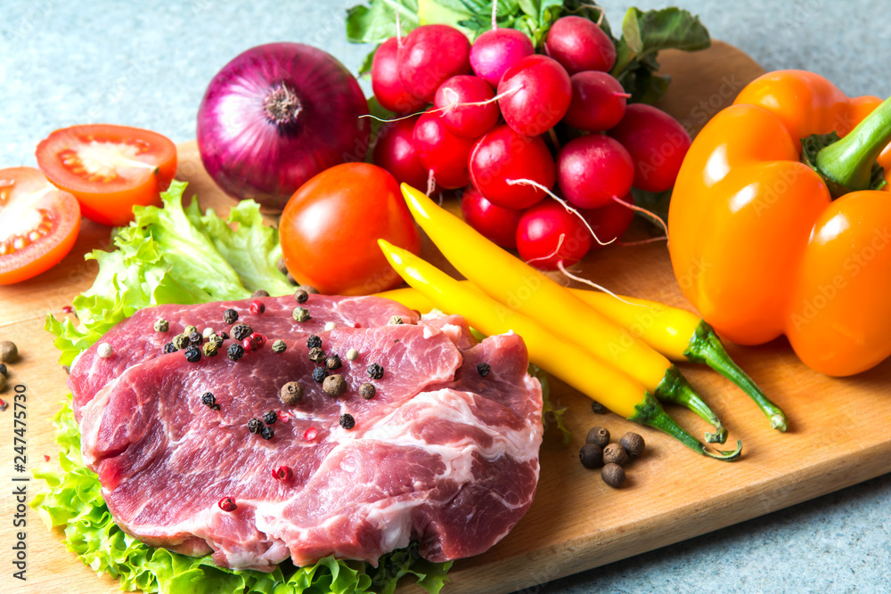 Pork-neck meat steaks on lettuce on background of radishes, tomato, red chili peppers, yellow chili peppers, green paprika, yellow paprika, red paprika, black pepper. Horizontal. Red onions, shallots