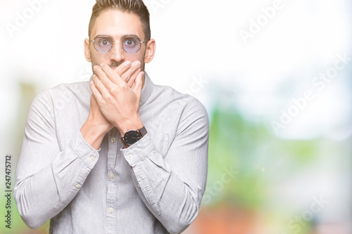 Young handsome man wearing sunglasses over isolated background shocked covering mouth with hands for mistake. Secret concept.