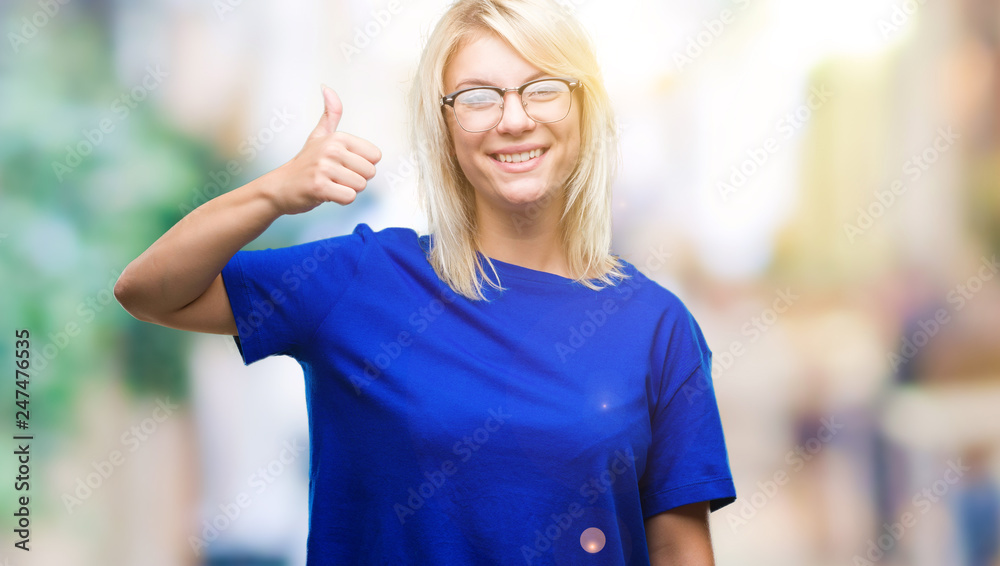 Young beautiful blonde woman wearing glasses over isolated background doing happy thumbs up gesture with hand. Approving expression looking at the camera with showing success.