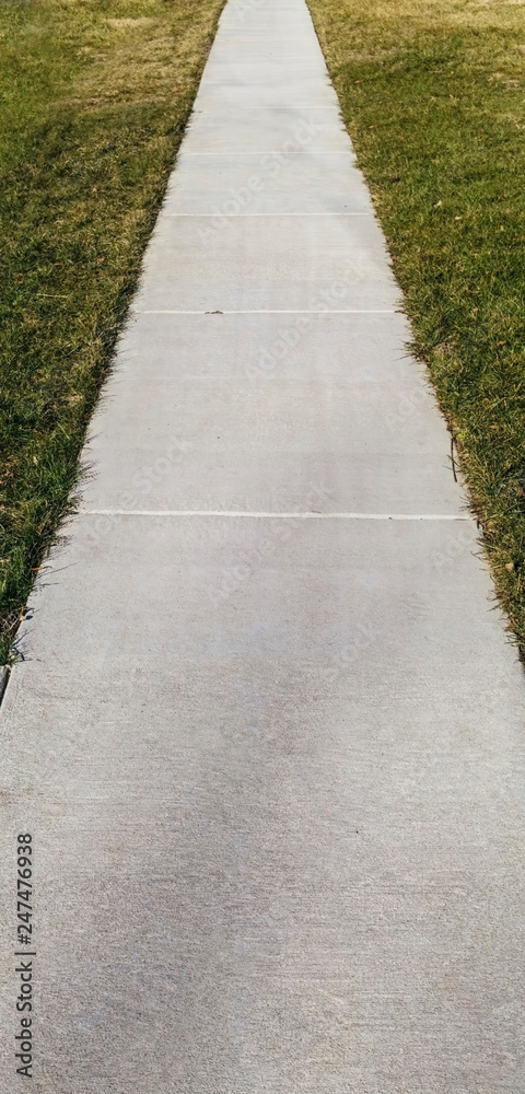 Perspective of neighborhood sidewalk flanked by grass.