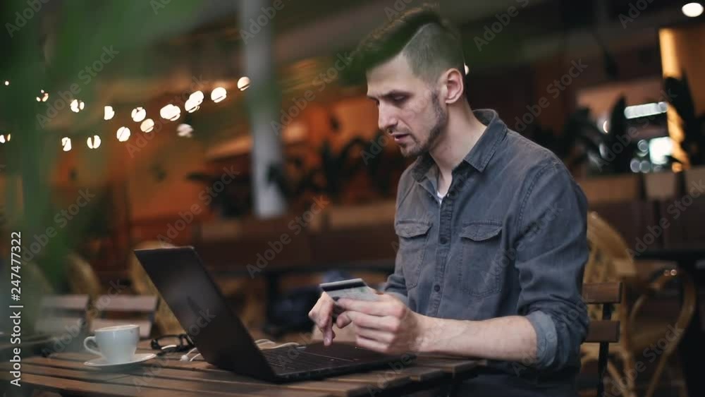 Man wearing casual outfit having shopping with his credit card, he typing numbers of his card on laptop and buy something while sitting at the cafe interior Man wearing casual outfit having shopping with his credit card, he typing numbers of his card on laptop and buy something while sitting at the cafe interior