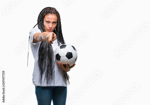 Young braided hair african american girl holding soccer ball over isolated background pointing with finger to the camera and to you, hand sign, positive and confident gesture from the front