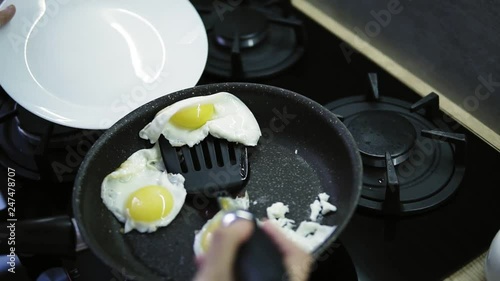 A woman's hands put the fryied eggs from the hot pan on the white plate. Late breakfast at home. Close up view photo