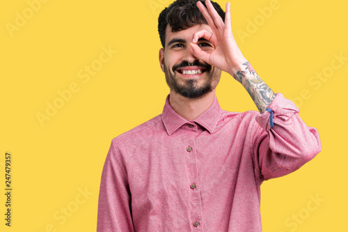 Young handsome man wearing pink shirt over isolated background doing ok gesture with hand smiling, eye looking through fingers with happy face.